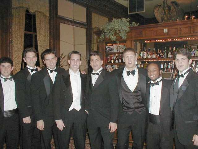 Friends wearing formal clothes gathered around a piano