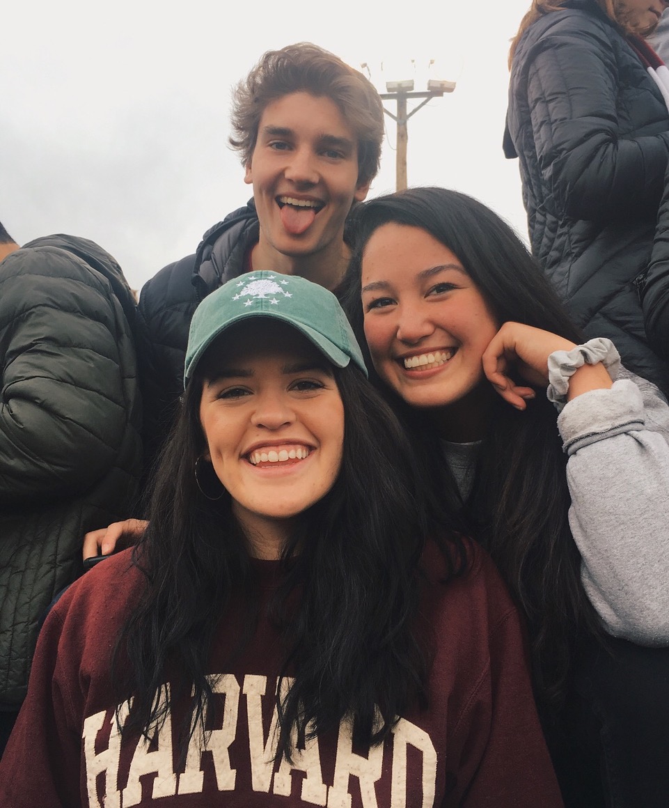 Three friends smiling together outdoors in Harvard clothing