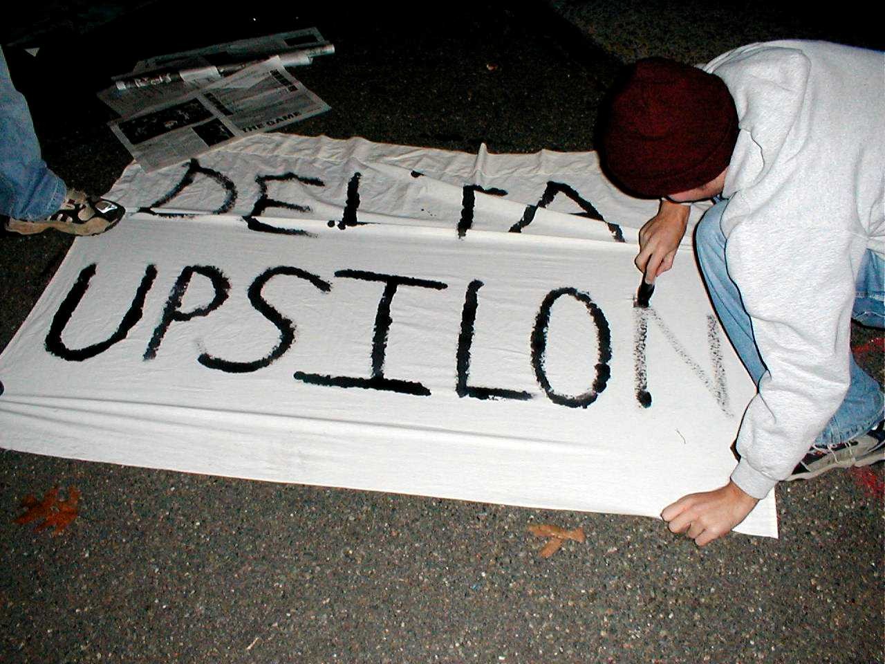 A person painting the words Delta Upsilon on a white banner