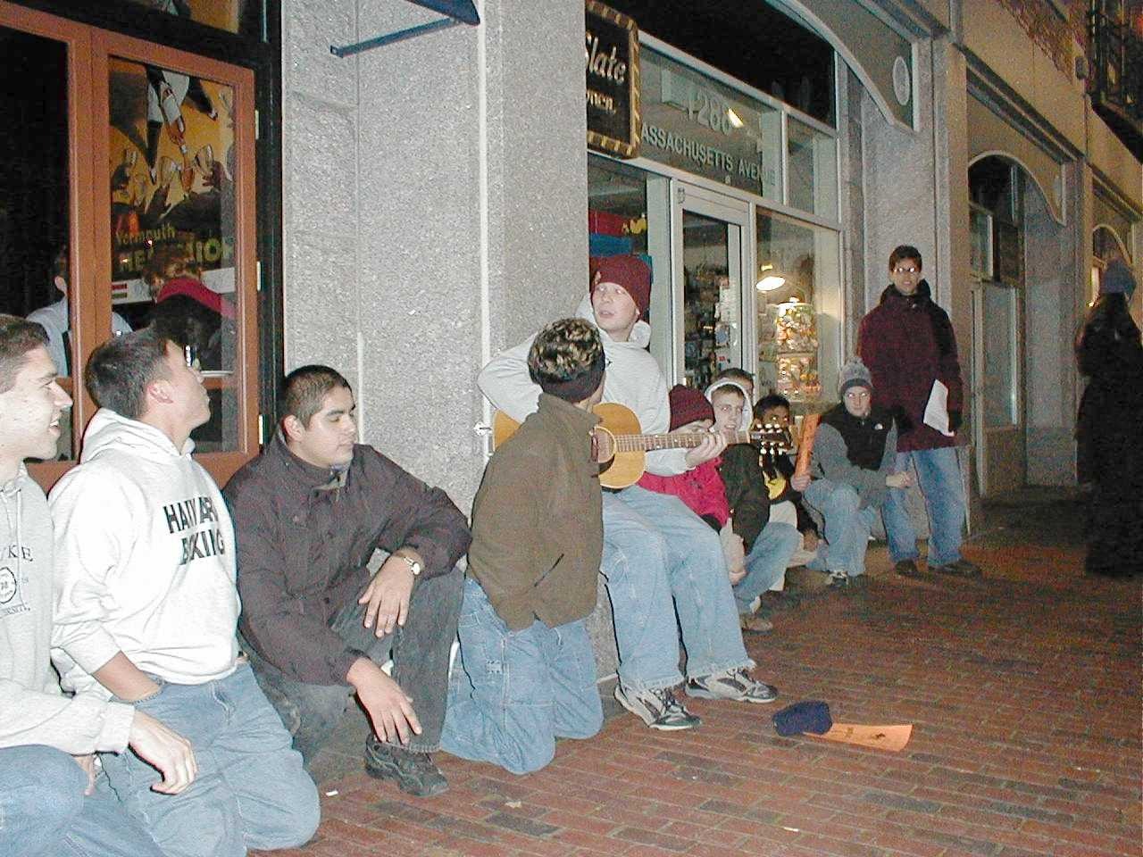 Friends sitting together outside a building as one plays a guitar