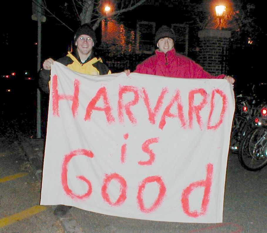 Two friends holding a hand-painted Harvard is Good sign